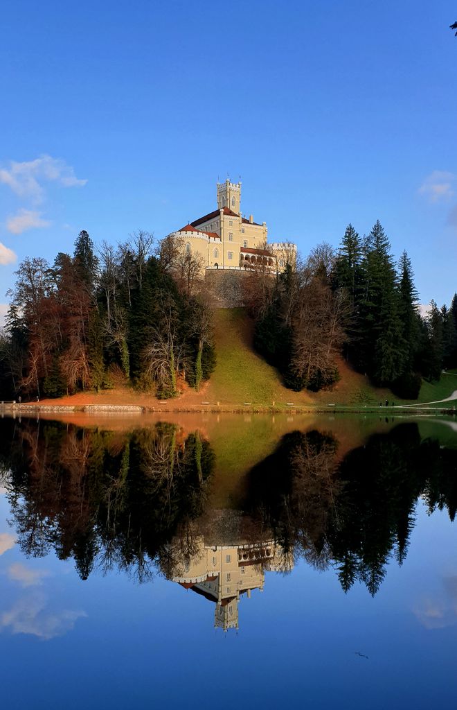 A striking castle perched on a hill, beautifully mirrored in a tranquil lake.